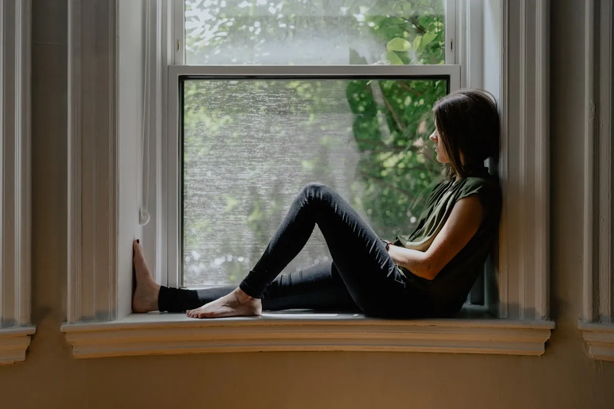 Mujer pensativa mirando por la ventana con expresión tranquila